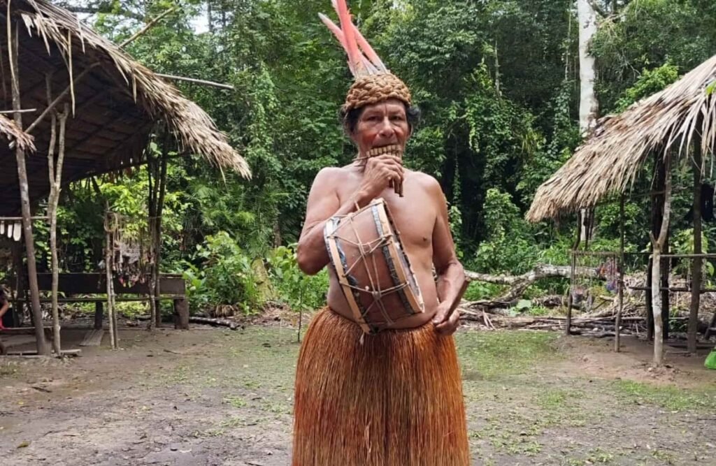 A yagua native person playing a zampoña and a drum.